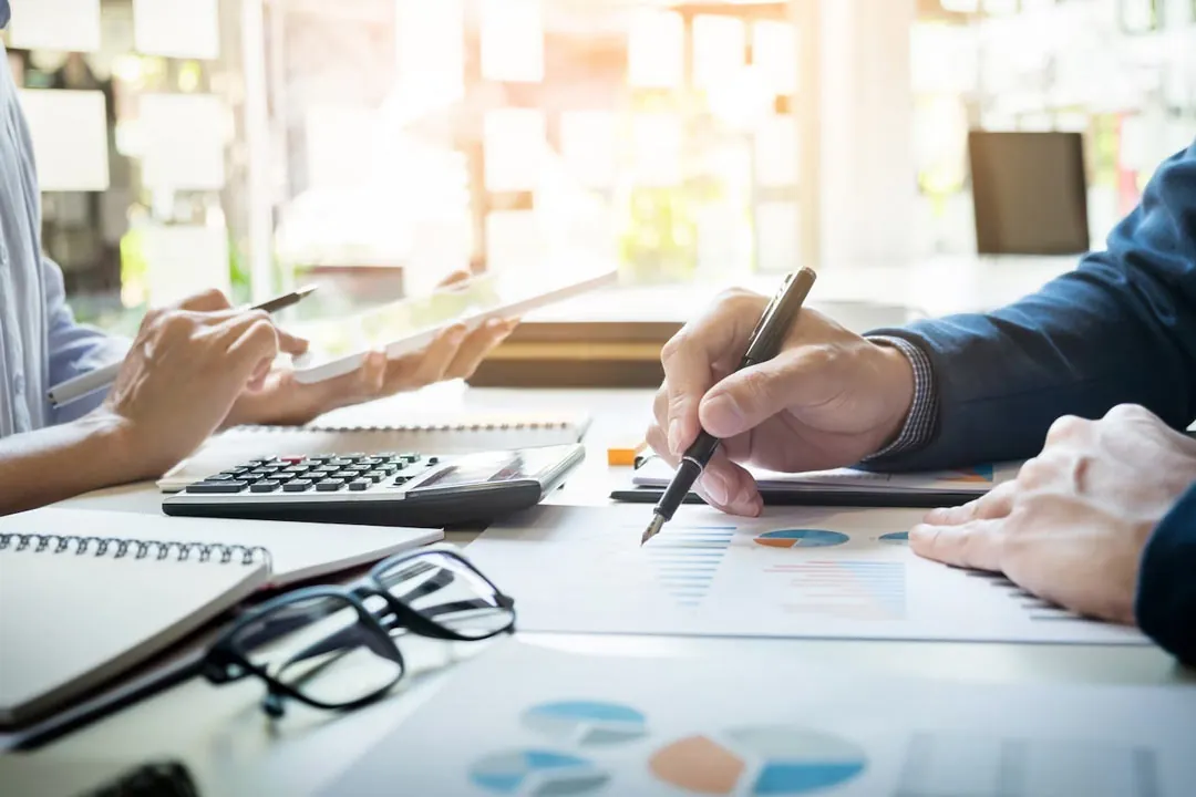 Mãos de um executivo analisando dados de gráficos impressos em folhas de sulfite na mesa do escritório