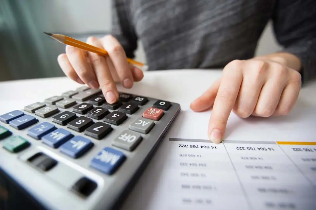 Las manos de una empresaria utilizando una calculadora para alimentar una hoja de cálculo con cifras de la empresa.