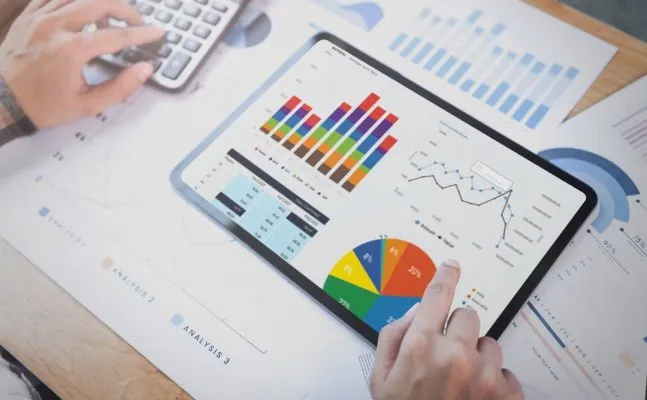 Parte da mão de um profissional de contabilidade apontando para a tela de um tablet que contém um dashboard com números e gráficos contábeis