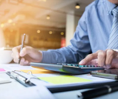 Executivo utilizando calculadora e anotando dados em mesa de escritório de contabilidade