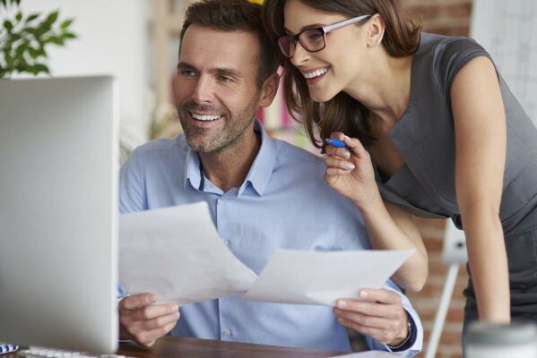 Happy man and woman analyzing accounts payable and receivable on computer