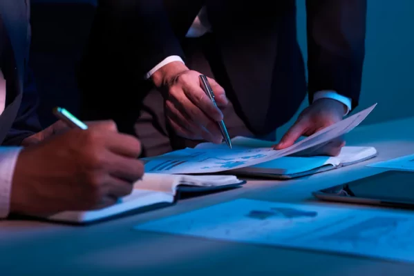 Two men holding a pen and writing down calculations in a notebook