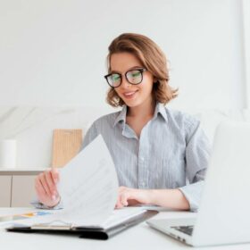 Mulher alegre de óculos lendo novo contrato enquanto trabalha