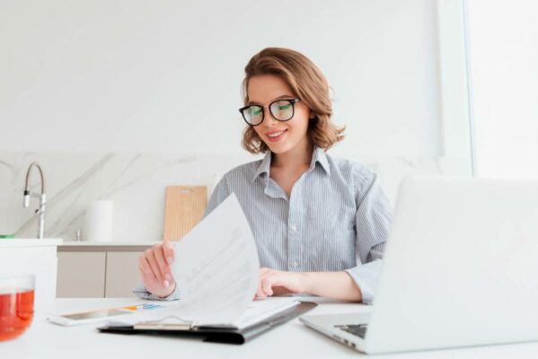 Mulher alegre de óculos lendo novo contrato enquanto trabalha