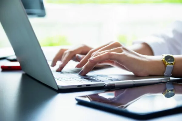 computador e celular em cima de uma mesa enquanto mulher digita buscando sobre holdings